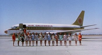 Movie still from “Smile” (1975), directed by Michael Ritchie – A group of women standing in front of an airplane; Extreme Wide shot, Low angle
