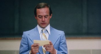 Movie still from “Smile” (1975), directed by Michael Ritchie – A man in a blue suit and yellow tie holding a piece of paper; Close Up shot, Low angle
