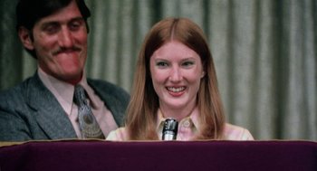 Movie still from “Smile” (1975), directed by Michael Ritchie – A woman smiles while sitting in front of a microphone in front of another man; Close Up shot, Low angle