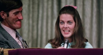 Movie still from “Smile” (1975), directed by Michael Ritchie – A woman with a pink bow in her hair is sitting at a table; Close Up shot, Low angle
