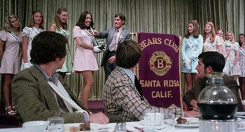 Movie still from “Smile” (1975), directed by Michael Ritchie – A group of young men and women standing in front of a bear club banner; Medium shot, Low angle