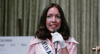 Movie still from “Smile” (1975), directed by Michael Ritchie – A woman in a pink dress is holding a microphone; Close Up shot, Low angle