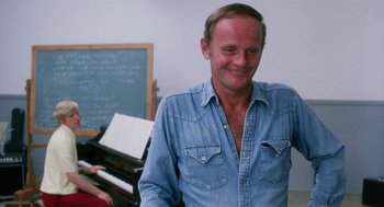 Movie still from “Smile” (1975), directed by Michael Ritchie – A man wearing a jean shirt standing in front of a chalkboard; Medium shot, Over the shoulder angle
