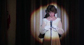Movie still from “Smile” (1975), directed by Michael Ritchie – A woman in a white dress holding a microphone; Medium shot, Low angle