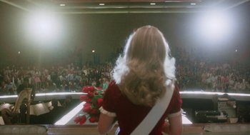 Movie still from “Smile” (1975), directed by Michael Ritchie – A woman in a red dress is holding a bouquet of roses; Medium shot, Low angle