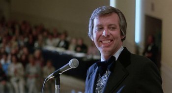 Movie still from “Smile” (1975), directed by Michael Ritchie – A man in a suit smiles while standing at a microphone; Close Up shot, Low angle