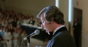 Movie still from “Smile” (1975), directed by Michael Ritchie – A man in a tuxedo is speaking into a microphone; Close Up shot, Low angle