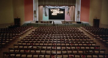 Movie still from “Smile” (1975), directed by Michael Ritchie – An empty auditorium with rows of seats and a large screen; Extreme Wide shot, High angle