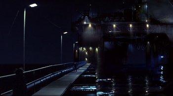 Movie still from “Smilla's Sense of Snow” (1997), directed by Bille August – A person walking on a sidewalk next to a body of water at night; Extreme Wide shot, Low angle
