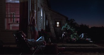 Movie still from “Smooth Talk” (1985), directed by Joyce Chopra – A man and a woman sitting on a chair in front of a house; Wide shot, Low angle
