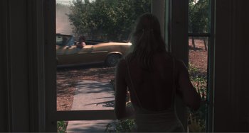 Movie still from “Smooth Talk” (1985), directed by Joyce Chopra – A woman standing in front of a window looking at a car; Wide shot, Over the shoulder angle