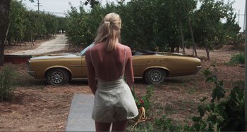 Movie still from “Smooth Talk” (1985), directed by Joyce Chopra – A woman standing in front of a yellow car; Wide shot, High angle