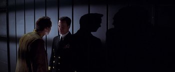 Movie still from “Snake Eyes” (1998), directed by Brian De Palma – A man in a suit and tie standing next to another man in a suit and tie; Medium shot, Low angle