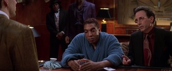 Movie still from “Snake Eyes” (1998), directed by Brian De Palma – A man sitting at a table in a blue robe; Medium shot, Over the shoulder angle