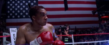 Movie still from “Snake Eyes” (1998), directed by Brian De Palma – A man wearing boxing gloves in a boxing ring; Medium shot, Low angle