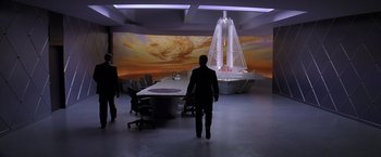 Movie still from “Snake Eyes” (1998), directed by Brian De Palma – A man in a suit walks in front of a projection of a ship; Extreme Wide shot, High angle