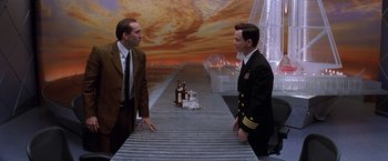 Movie still from “Snake Eyes” (1998), directed by Brian De Palma – Two men in suits are standing in front of a sky background; Medium shot, Low angle