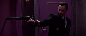 Movie still from “Snake Eyes” (1998), directed by Brian De Palma – A man holding a gun in front of a purple wall; Close Up shot, Low angle