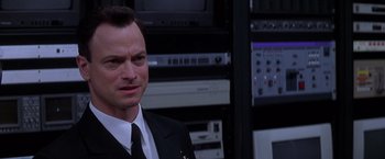 Movie still from “Snake Eyes” (1998), directed by Brian De Palma – A man wearing a suit and tie standing in a room; Close Up shot, Low angle