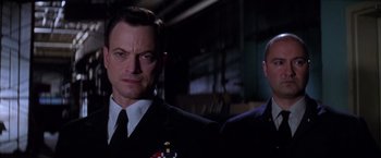 Movie still from “Snake Eyes” (1998), directed by Brian De Palma – A man in a suit and tie standing next to another man in a suit and tie; Close Up shot, Low angle