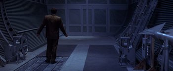 Movie still from “Snake Eyes” (1998), directed by Brian De Palma – A man in a brown suit walking down a hall way; Wide shot, Low angle