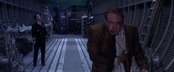 Movie still from “Snake Eyes” (1998), directed by Brian De Palma – A man with blood on his face is standing in a room; Medium shot, Low angle