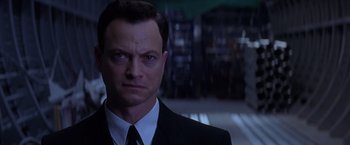 Movie still from “Snake Eyes” (1998), directed by Brian De Palma – A man in a suit and tie in front of a building; Close Up shot, Low angle