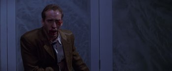 Movie still from “Snake Eyes” (1998), directed by Brian De Palma – A man with blood on his face is sitting in front of a white door; Medium shot, High angle