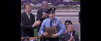 Movie still from “Snake Eyes” (1998), directed by Brian De Palma – A police officer is holding a plaque in front of a group of people; Medium shot, Over the shoulder angle