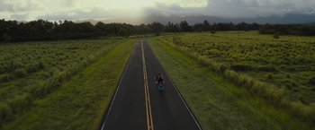 Movie still from “Snatched” (2017), directed by Jonathan Levine – A person riding a motorcycle down the middle of a road; Extreme Wide shot, High angle