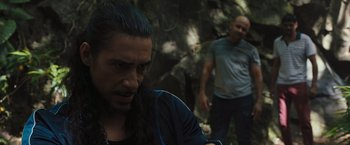 Movie still from “Snatched” (2017), directed by Jonathan Levine – A man with long black hair is looking at the camera while another man stands in the background; Medium shot, Over the shoulder angle