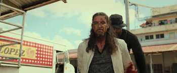 Movie still from “Snatched” (2017), directed by Jonathan Levine – A man with long black hair and a red bandage on his face; Medium shot, Low angle