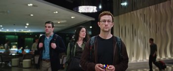 Movie still from “Snowden” (2016), directed by Oliver Stone – A man holding a rubik's cube while standing next to two other people; Medium shot, Over the shoulder angle