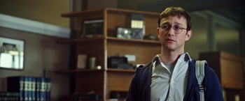 Movie still from “Snowden” (2016), directed by Oliver Stone – A man with glasses is standing in front of a bookshelf; Close Up shot, Over the shoulder angle