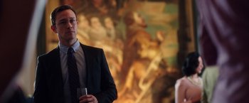 Movie still from “Snowden” (2016), directed by Oliver Stone – A man standing in front of a painting holding a wine glass; Medium shot, Over the shoulder angle