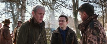 Movie still from “Snowden” (2016), directed by Oliver Stone – Two men standing next to each other near a tree; Medium shot, Over the shoulder angle