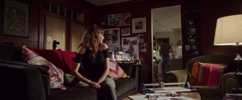 Movie still from “Snowden” (2016), directed by Oliver Stone – A woman sitting on top of a couch in a living room; Wide shot, Over the shoulder angle