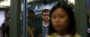Movie still from “Snowden” (2016), directed by Oliver Stone – A man in a suit and glasses is in a glass case; Close Up shot, Over the shoulder angle