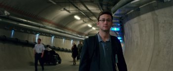 Movie still from “Snowden” (2016), directed by Oliver Stone – A man in a suit standing in an underground tunnel; Medium shot, Over the shoulder angle