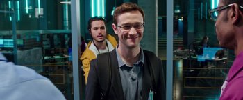 Movie still from “Snowden” (2016), directed by Oliver Stone – A man in a suit and tie standing next to another man in a suit; Medium shot, Over the shoulder angle