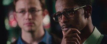 Movie still from “Snowden” (2016), directed by Oliver Stone – A man with glasses is looking at the camera while another man looks on; Close Up shot, Over the shoulder angle