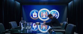 Movie still from “Snowden” (2016), directed by Oliver Stone – A man sitting at a table in front of the cia logo; Wide shot, Low angle
