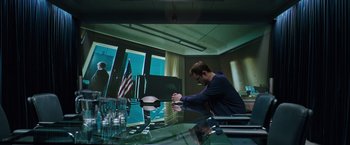 Movie still from “Snowden” (2016), directed by Oliver Stone – A man sitting at a table in front of an american flag; Wide shot, Low angle