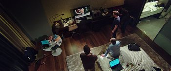 Movie still from “Snowden” (2016), directed by Oliver Stone – Three men are sitting in front of a television; Wide shot, High angle