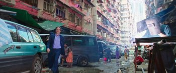 Movie still from “Snowden” (2016), directed by Oliver Stone – A man walking down a street with a van in front of a building; Wide shot, Over the shoulder angle