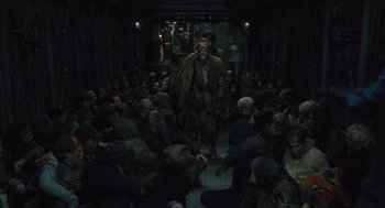 Movie still from “Snowpiercer” (2013), directed by Bong Joon Ho – A group of people sitting in a dark room; Wide shot, High angle