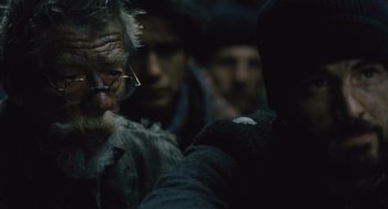 Movie still from “Snowpiercer” (2013), directed by Bong Joon Ho – An old man with a beard wearing glasses and wearing a hat; Close Up shot, Over the shoulder angle