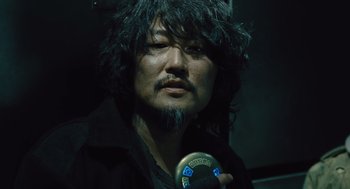 Movie still from “Snowpiercer” (2013), directed by Bong Joon Ho – A man with long black hair holding a microphone; Close Up shot, Over the shoulder angle