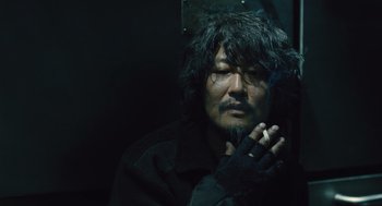 Movie still from “Snowpiercer” (2013), directed by Bong Joon Ho – A man with long black hair is smoking a cigarette; Close Up shot, Low angle