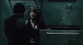Movie still from “Snowpiercer” (2013), directed by Bong Joon Ho – A man in a black jacket is standing next to another man in a black jacket; Medium shot, Over the shoulder angle